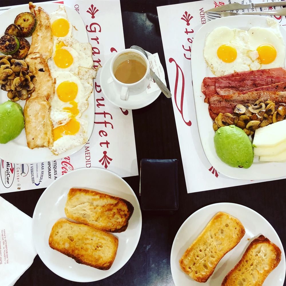 Mesa de desayuno con huevos, beicon, setas, aguacate, tostadas y café sobre manteles de Gran Buffet